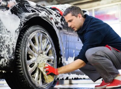 Hombre lavando un auto con una esponja, utilizando productos de línea automotriz para un acabado brillante.
